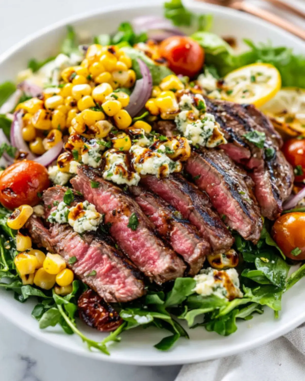 Balsamic steak gorgonzola salad with grilled corn, cherry tomatoes, red onion, and creamy blue cheese on a white plate