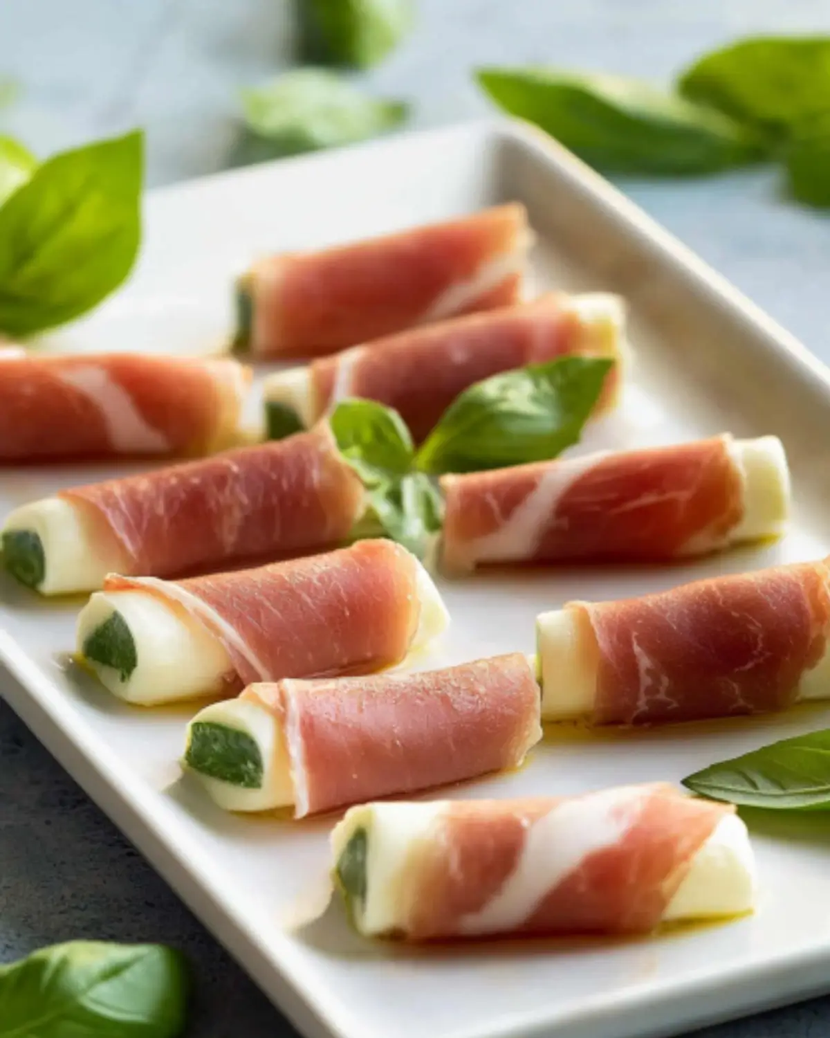 Mozzarella wrapped with prosciutto and fresh basil leaves on a clean white plate.