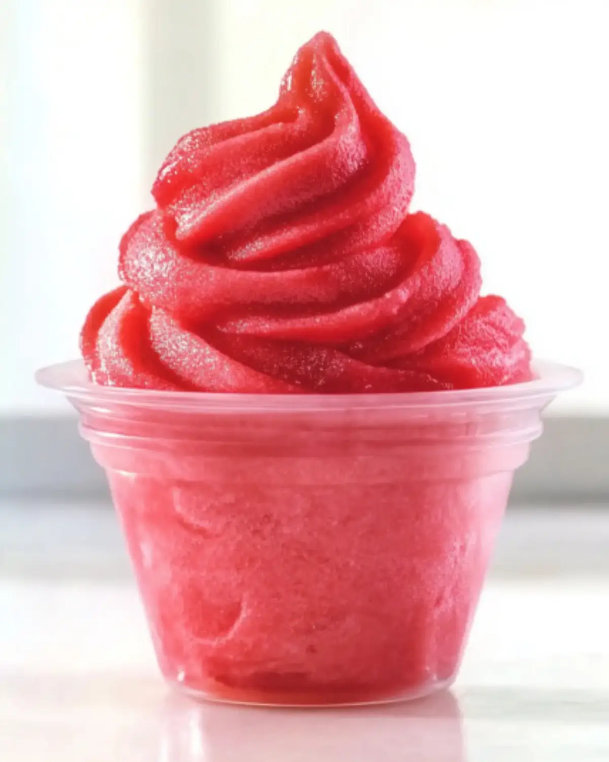 Swirled strawberry Dole Whip in a clear plastic cup with smooth texture and vibrant color.