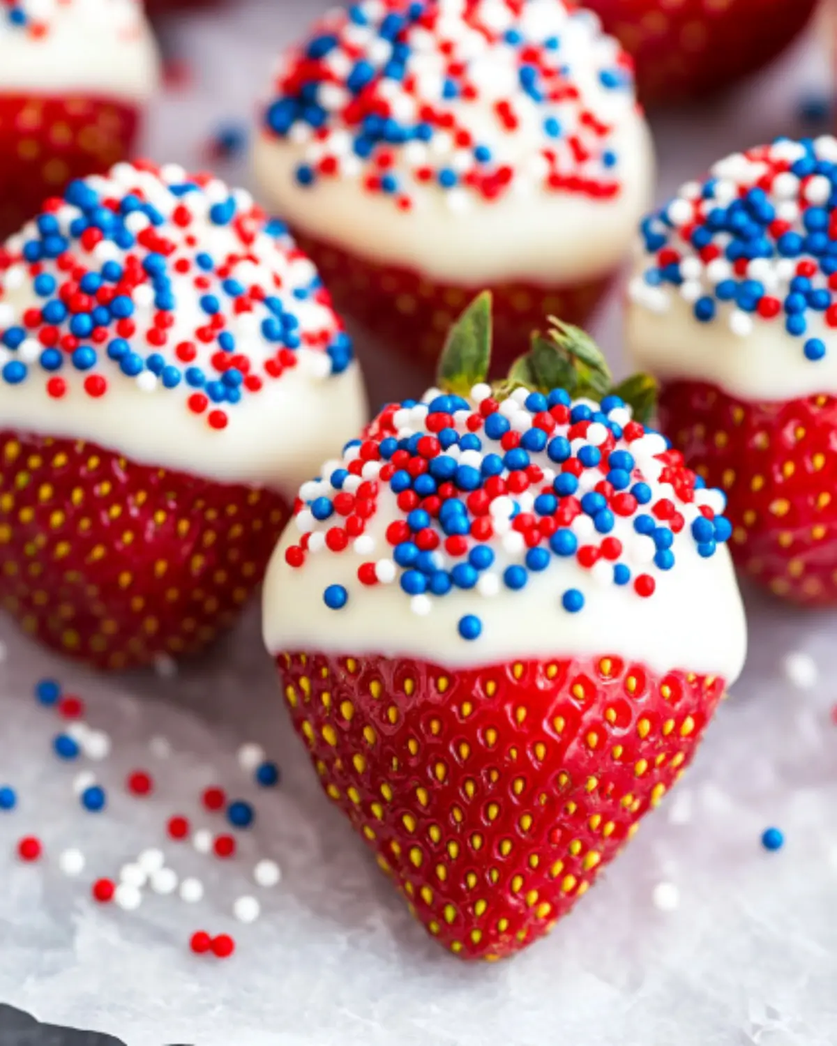 Close-up of chocolate-covered strawberries decorated with red, white, and blue nonpareil sprinkles, perfect for 4th of July.