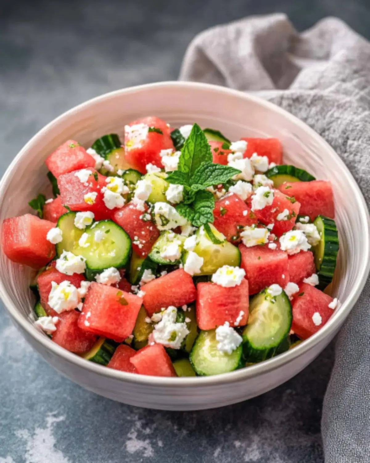 A fresh and vibrant bowl of Watermelon Salad With Cucumber And Feta, garnished with mint, featuring cubes of watermelon, cucumber, and feta.