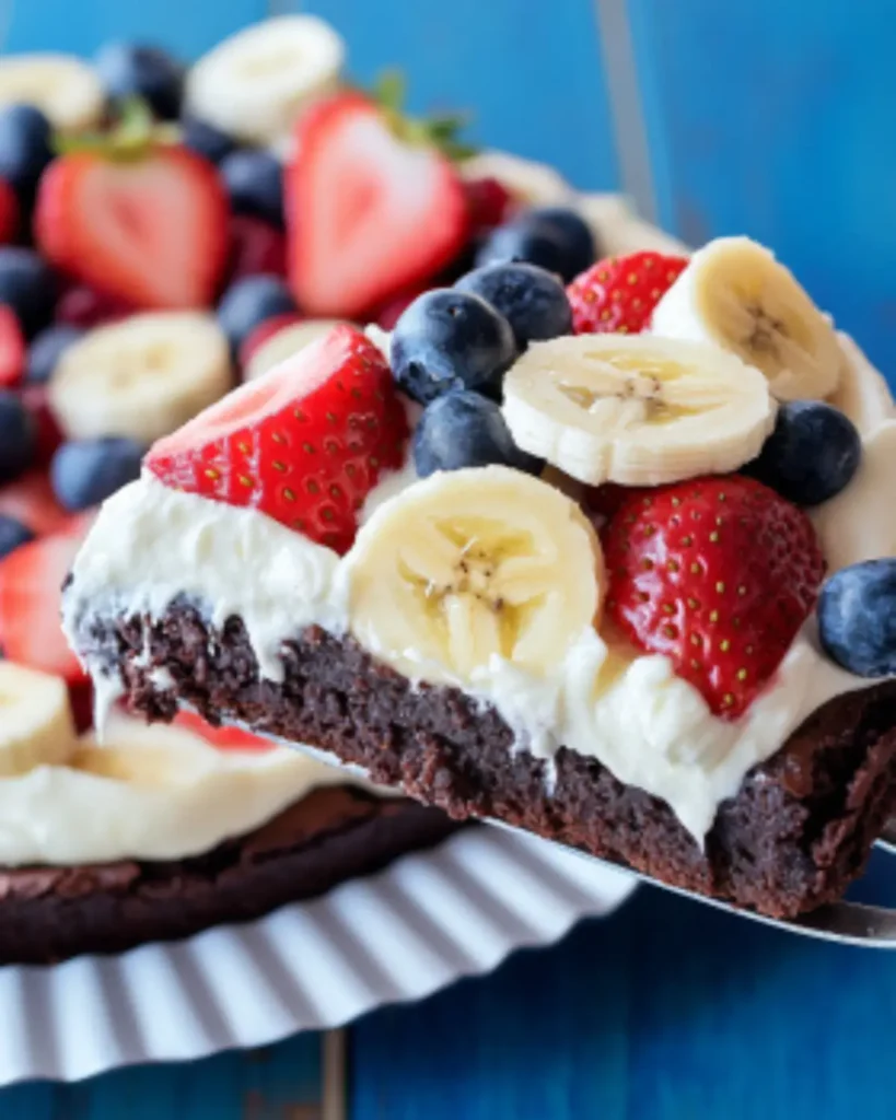 Overhead view of brownie dessert pizza topped with strawberries, bananas, and blueberries, sliced into wedges.