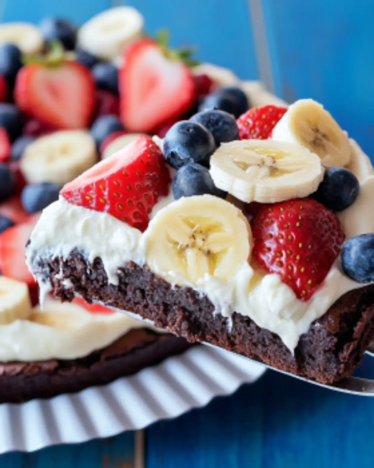 Overhead view of brownie dessert pizza topped with strawberries, bananas, and blueberries, sliced into wedges.