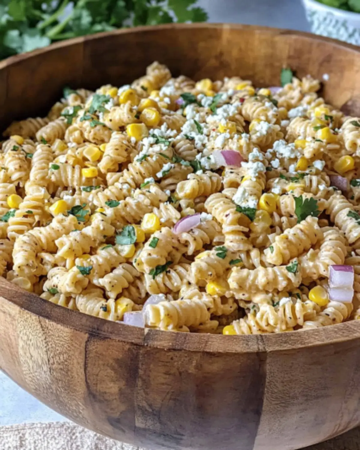 Close-up of creamy Elote Pasta Salad with corn, red onion, cotija cheese, and cilantro in a wooden bowl.