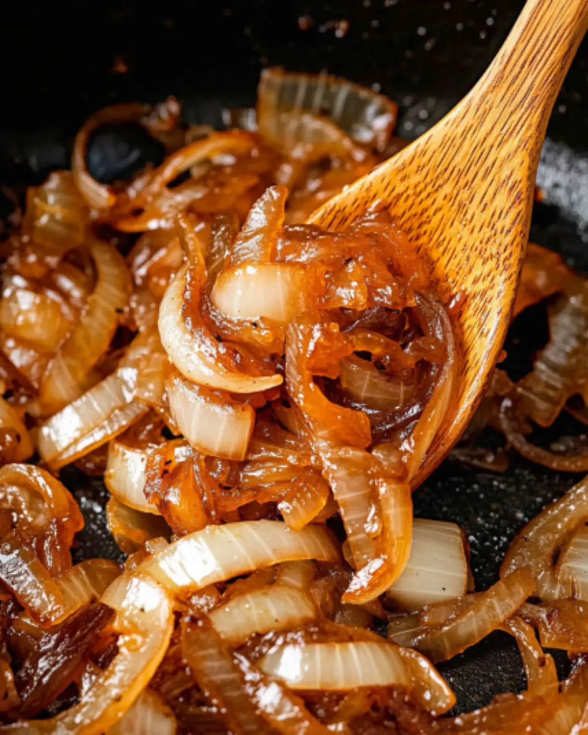 Homemade caramelized onions in a nonstick skillet, stirred with a wooden spoon, soft and browned to perfection.