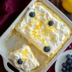 Lemon pudding poke cake with whipped topping, blueberries, and lemon zest in a white baking dish