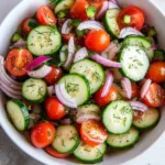 Fresh cucumber tomato salad with red onion, cherry tomatoes, dill, and olive oil in a white bowl
