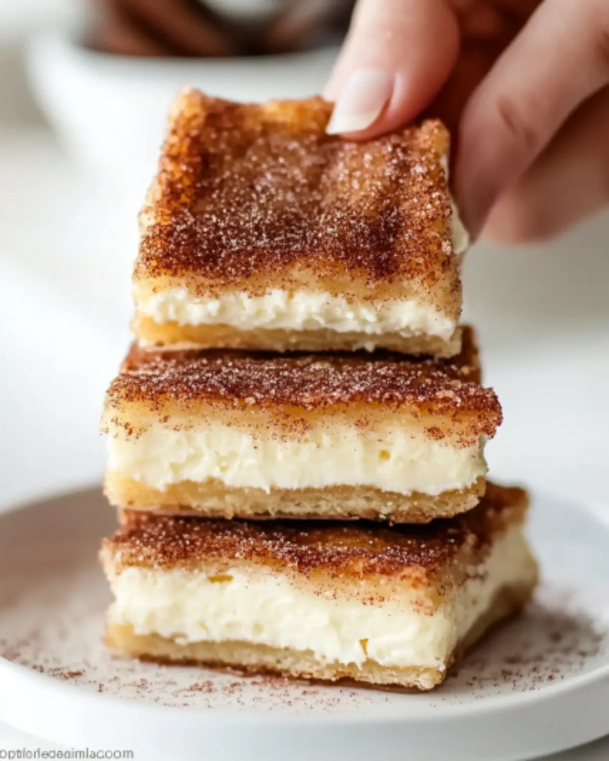 Close-up of flaky Churro Cheesecake Bars stacked on a white plate with cinnamon sticks, perfect for an easy cinnamon dessert.