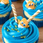 Gone Fishing Cupcakes with blue frosting, striped candy fishing poles, goldfish candy toppers, and yellow sprinkles on wood background