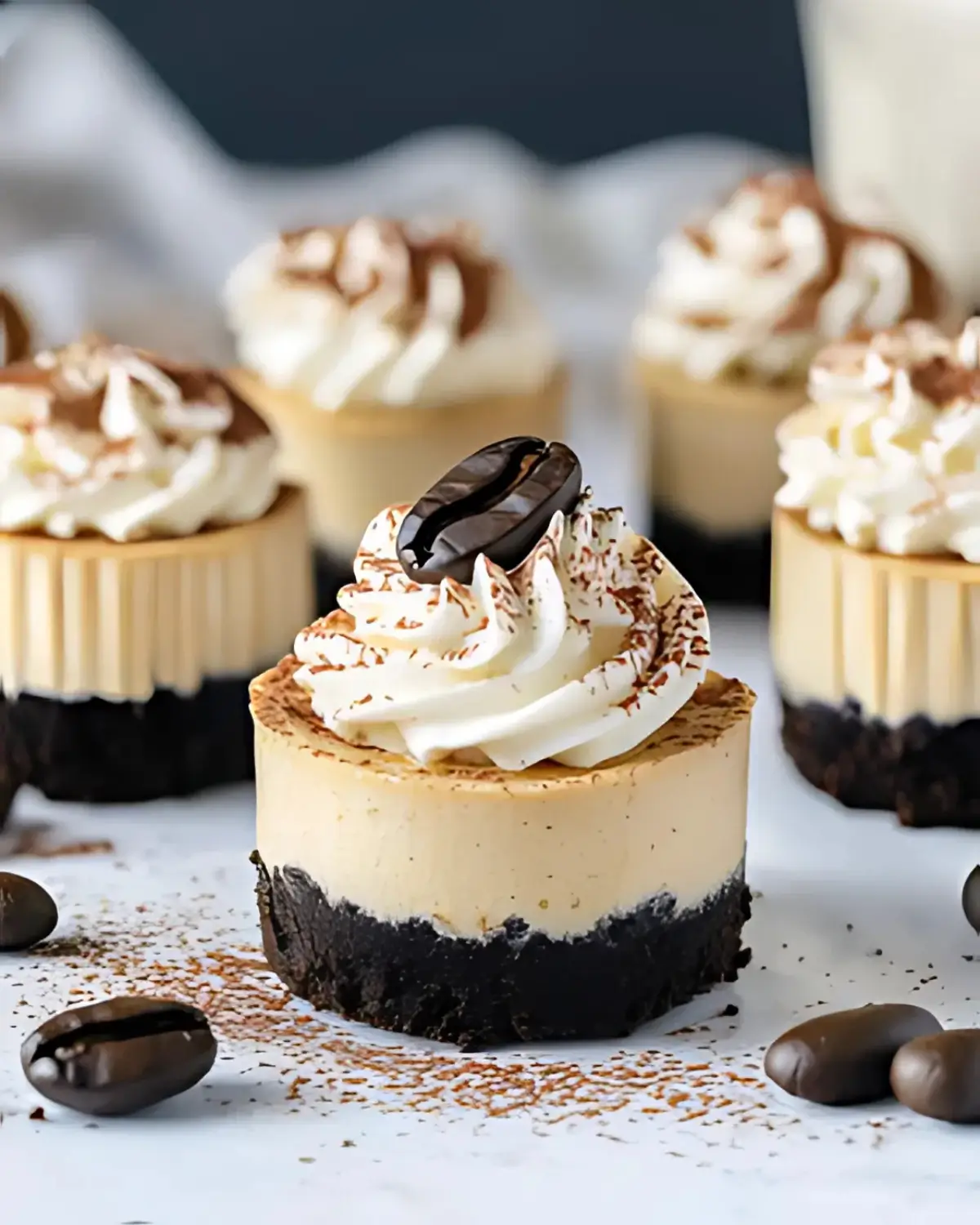 Mini coffee cheesecake topped with whipped cream, cocoa powder, espresso bean, Oreo crust, gold fork in background