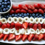 Fresh strawberries and blueberries arranged in a patriotic American flag pattern on a white platter for 4th of July.