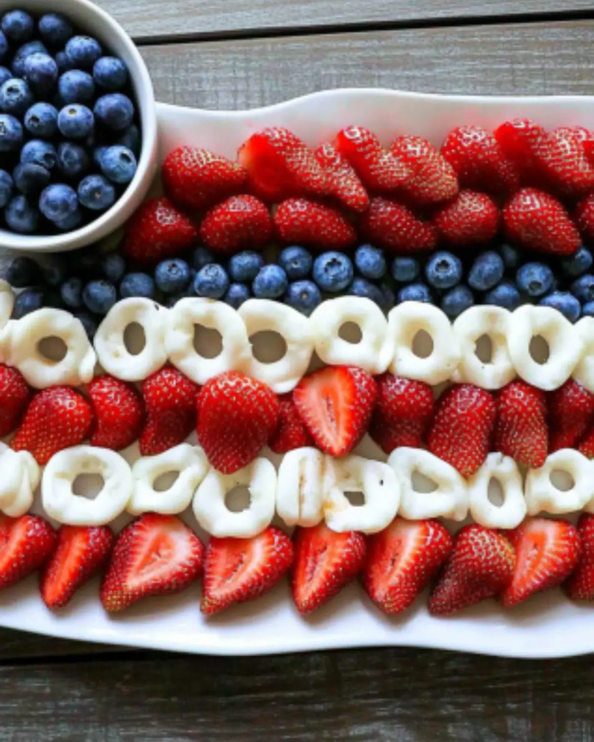 Fresh strawberries and blueberries arranged in a patriotic American flag pattern on a white platter for 4th of July.