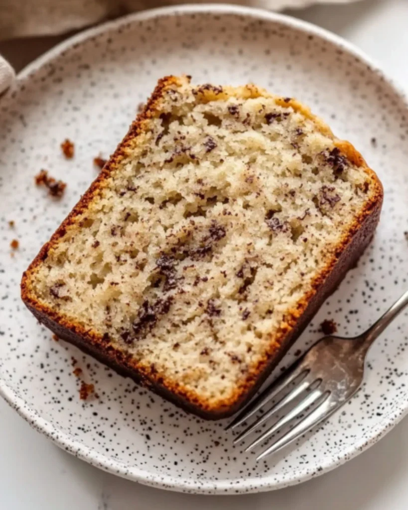 Close-up of a slice of banana bread on a speckled plate with a bite on a fork