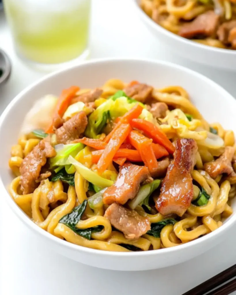 Yaki Udon stir-fry with pork, vegetables, and pickled ginger served in a white bowl with chopsticks