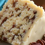 Close-up of a fluffy butter pecan cake slice with creamy frosting and chopped pecans, highlighting the cake’s moist texture.