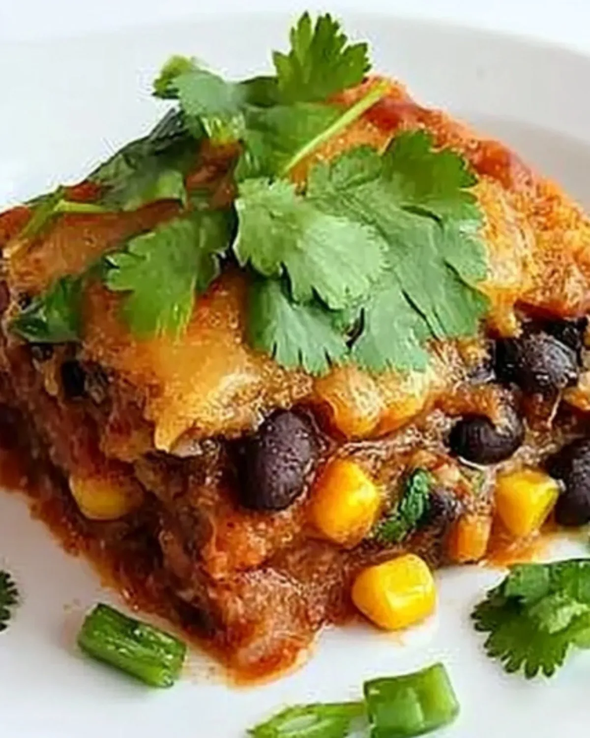 A serving of vegetarian Mexican fajita cornbread casserole topped with enchilada sauce, melted cheese, and fresh cilantro on a white plate.