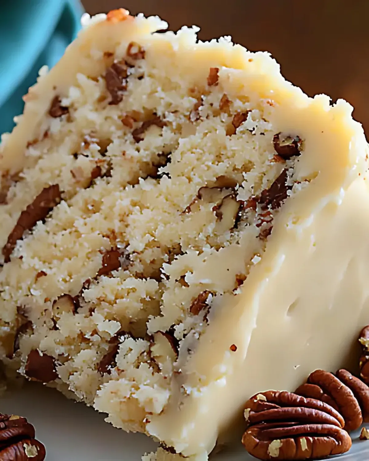 Close-up of a fluffy butter pecan cake slice with creamy frosting and chopped pecans, highlighting the cake’s moist texture.