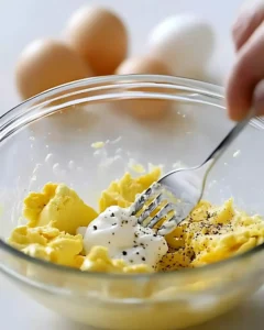 Mashed egg yolks with mayonnaise, mustard, and black pepper in a glass bowl with fork