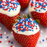 Close-up of a chocolate-covered strawberry with white chocolate and red, white, and blue sprinkles on white paper.