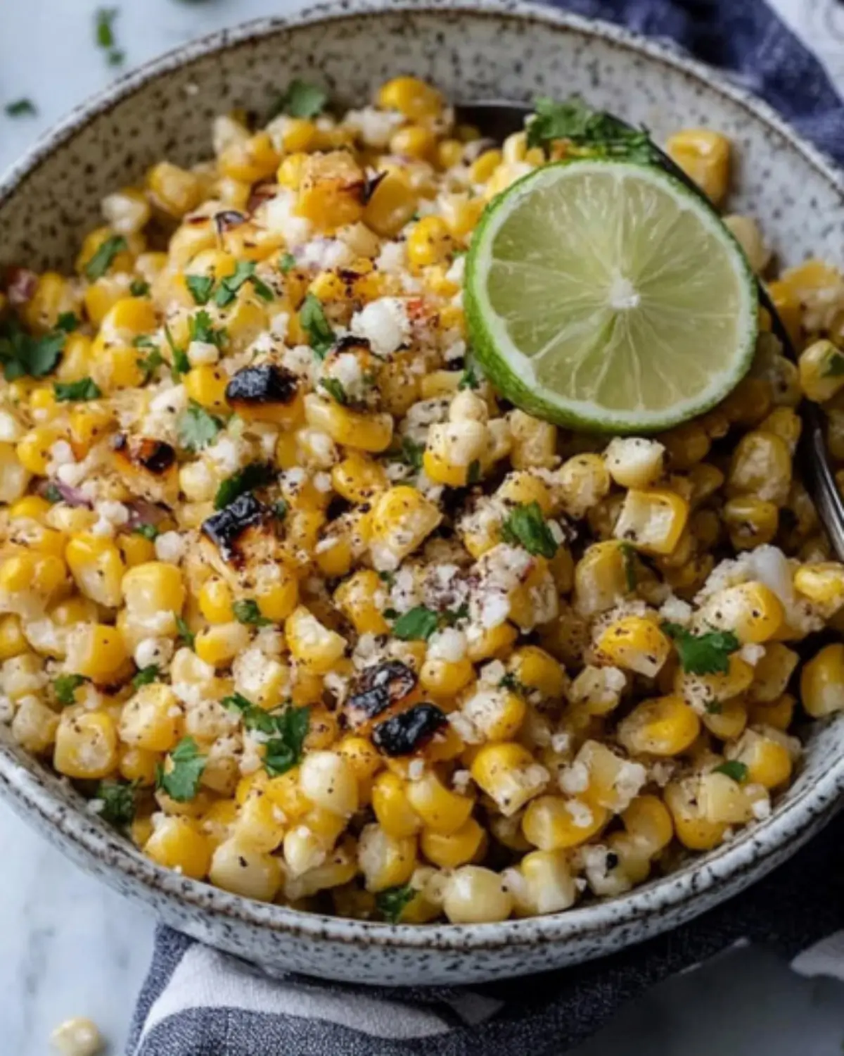 Mexican-style street corn in a speckled bowl with lime and cilantro