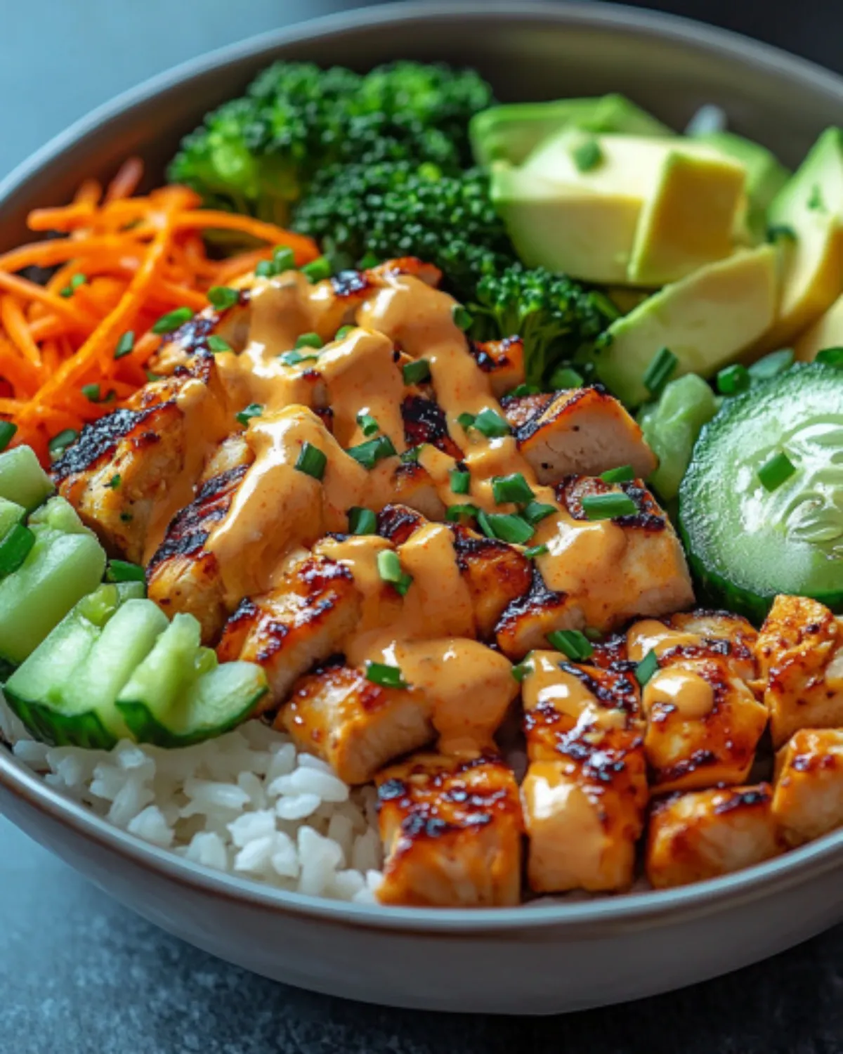 Bang Bang Chicken Bowl with spicy mayo, grilled chicken, avocado, broccoli, rice, and carrots in a ceramic bowl