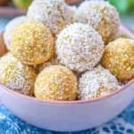 Bowl of no-bake lemon coconut energy balls, coated with shredded coconut, served on a blue napkin.
