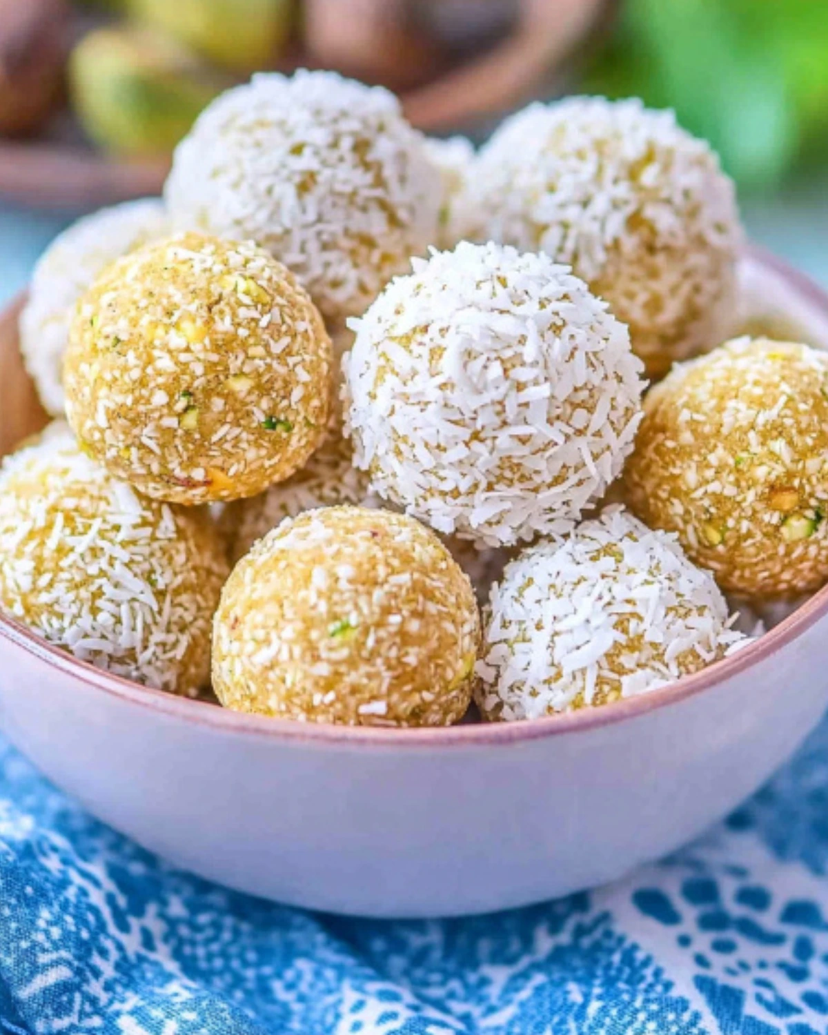 Bowl of no-bake lemon coconut energy balls, coated with shredded coconut, served on a blue napkin.