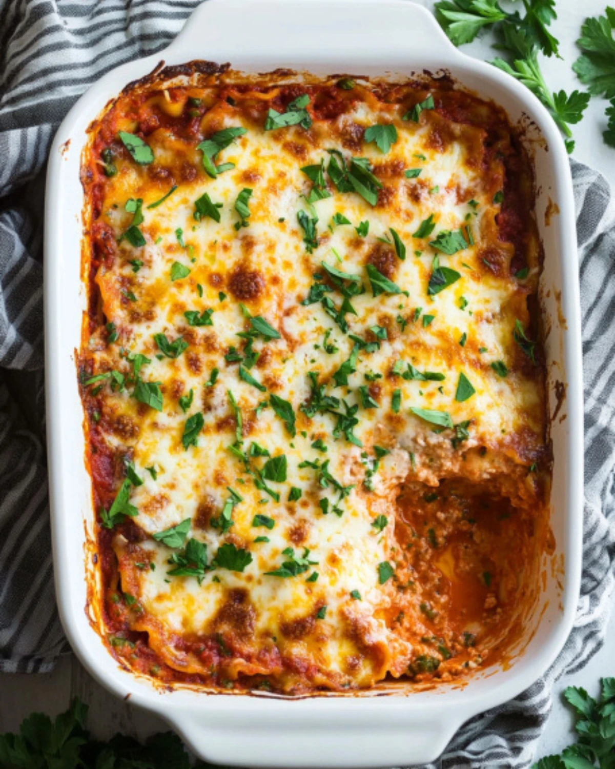 Baked cheesy lasagna in a white rectangular dish with fresh parsley topping