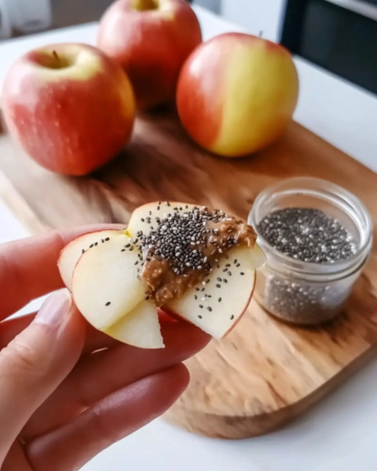 Sliced red apples on a white plate with a jar of nut butter and whole apples on a wooden cutting board