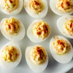 Plated deviled eggs with creamy filling and paprika garnish arranged on white serving dish