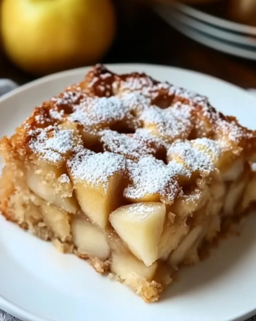 Close-up of a moist apple cake slice topped with powdered sugar and tender apple chunks