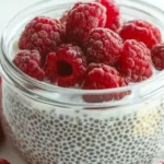 Fresh berries, Greek yogurt, chia seeds, honey, and granola arranged as parfait ingredients on a white surface.