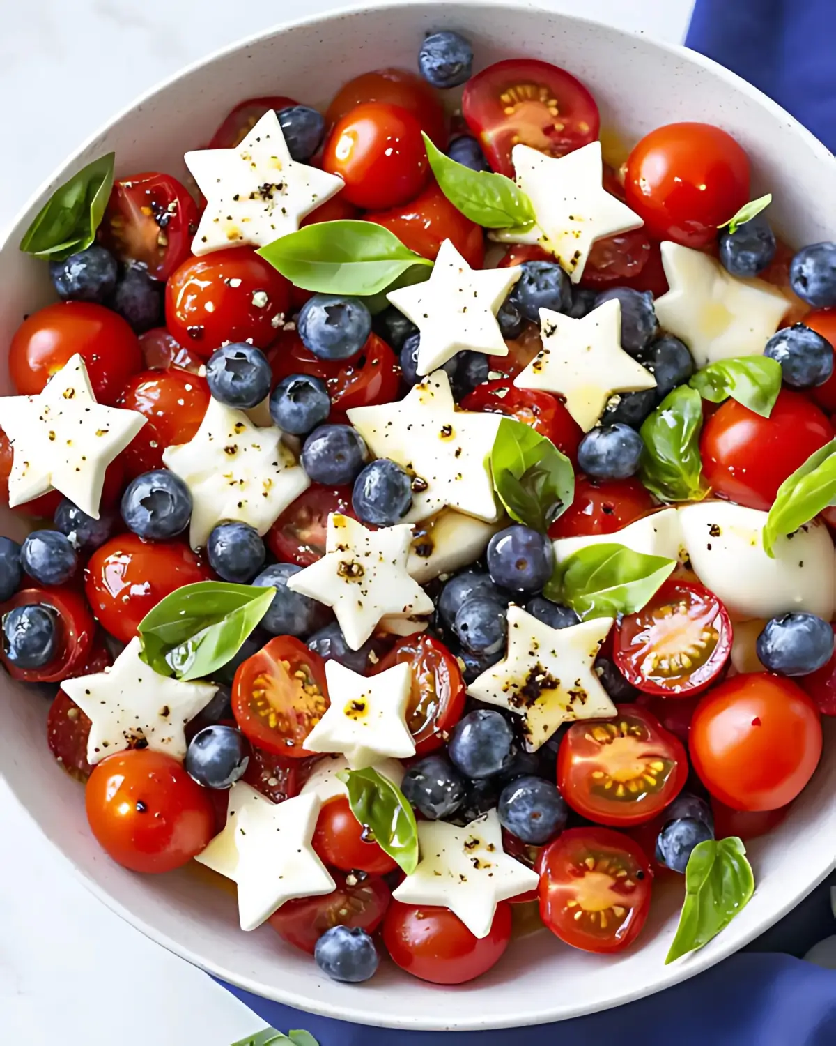 Fourth of July salad with cherry tomatoes, blueberries, mozzarella stars, and fresh basil in a white bowl