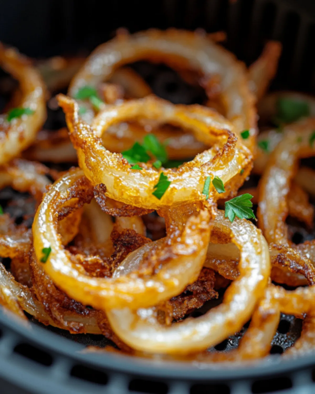 Golden air fryer crispy onions in a black air fryer basket, garnished with fresh parsley