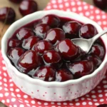 Close-up of homemade cherry pie filling in a bowl with a spoon and whole cherries