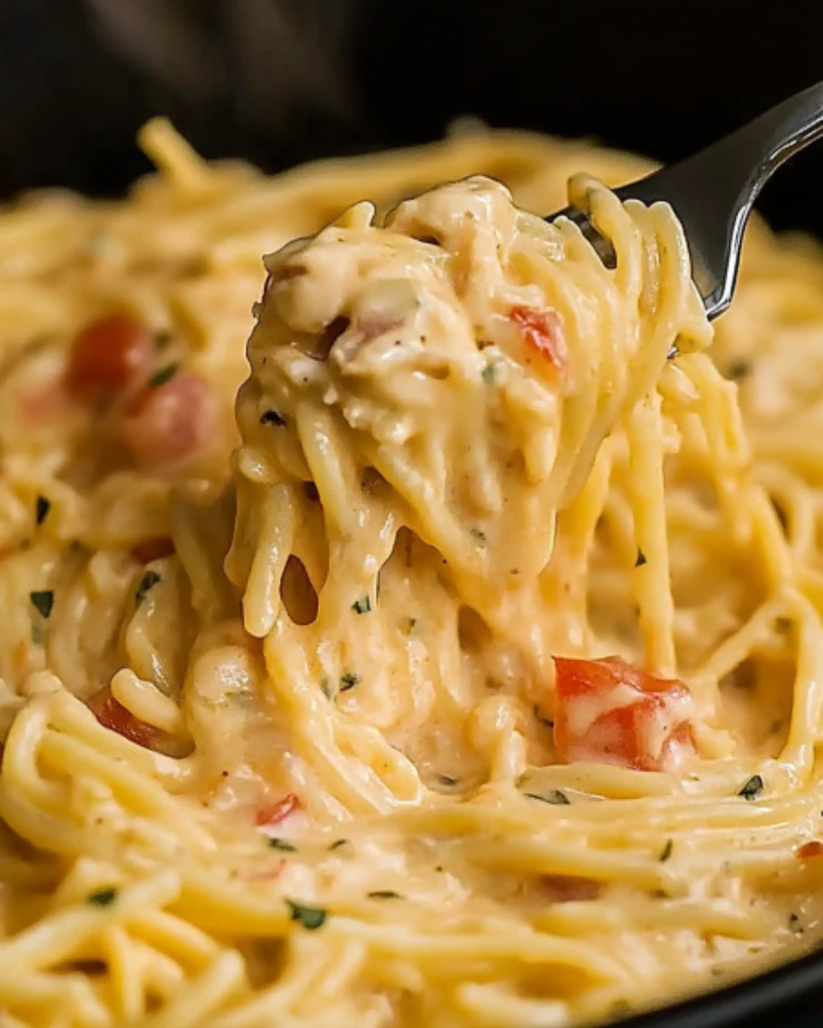 Close-up of cheesy CrockPot chicken spaghetti twirled on a fork with visible chunks of tomato and herbs.