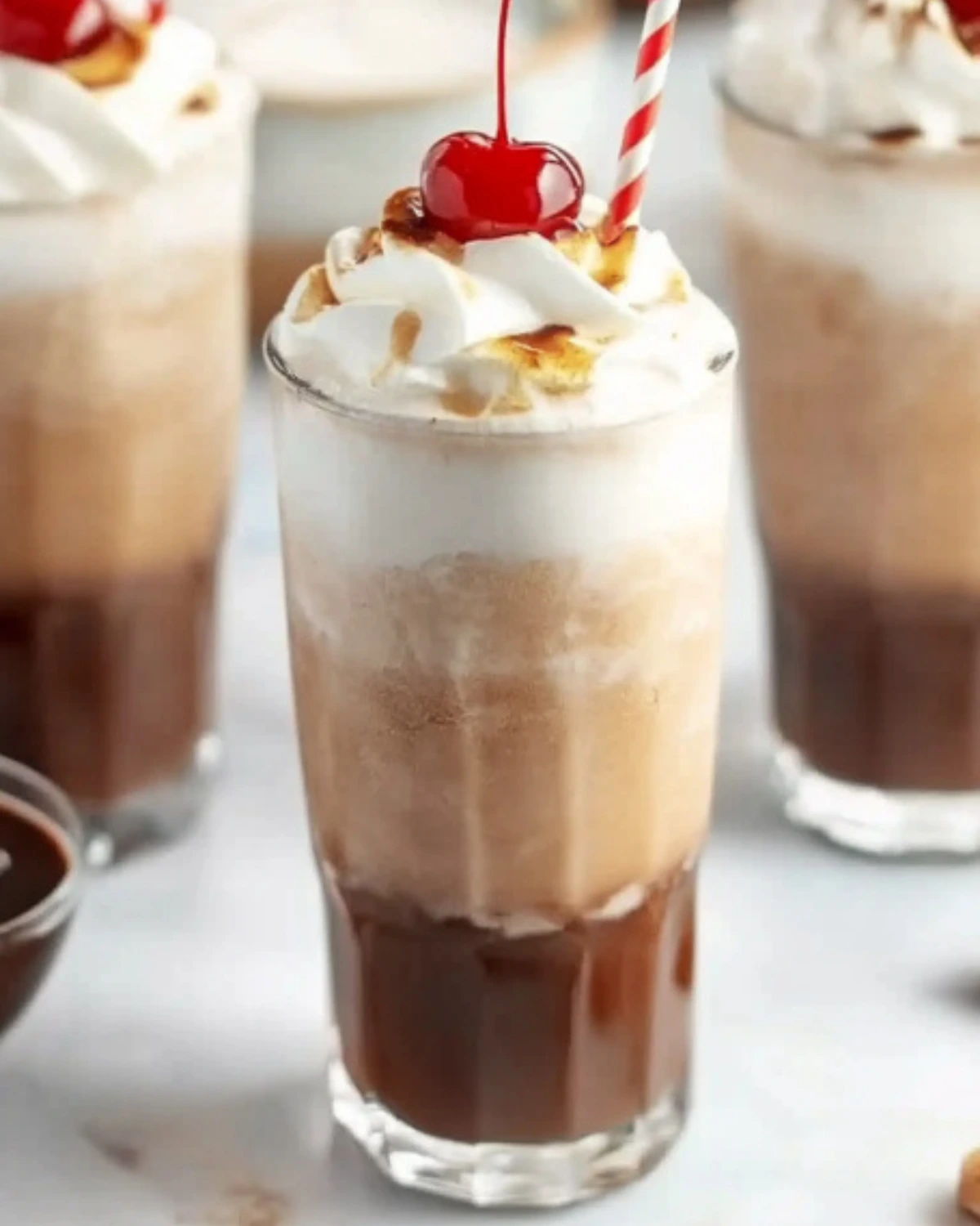Tall glass of chocolate Italian cream soda with whipped cream, cherry, and red-striped straw on a white surface.