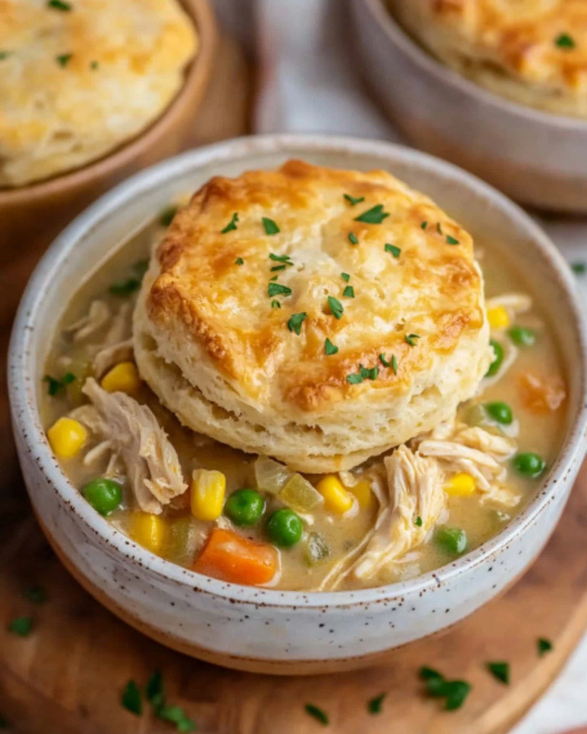 Slow cooker chicken pot pie in two bowls with golden flaky biscuits and colorful veggies