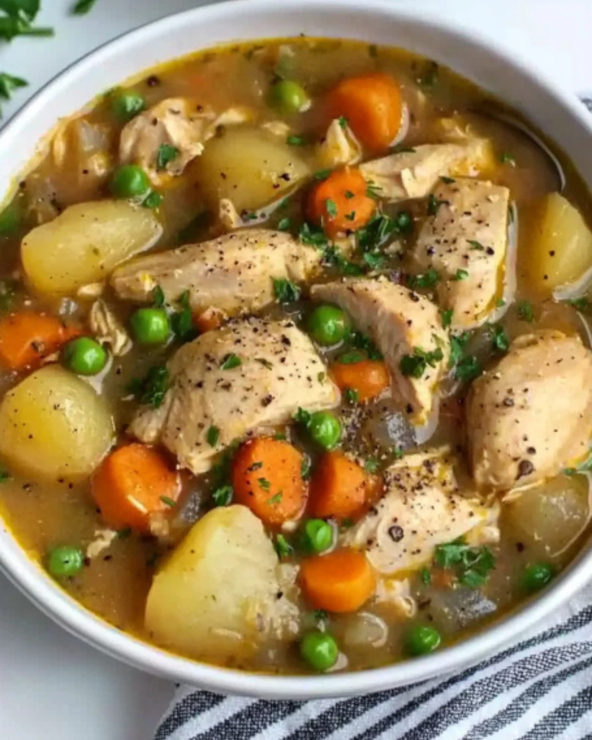 Overhead view of rustic chicken stew with carrots, peas, and potatoes in a white bowl