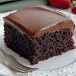 Square slice of moist chocolate cake with thick chocolate frosting on white plate and vintage fork