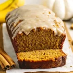 Front view of moist pumpkin banana bread with maple glaze, sliced and displayed with bananas and cinnamon sticks for a cozy fall recipe look