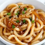 Udon noodles tossed with garlic soy sauce, caramelized onions, and fresh chives in a wok