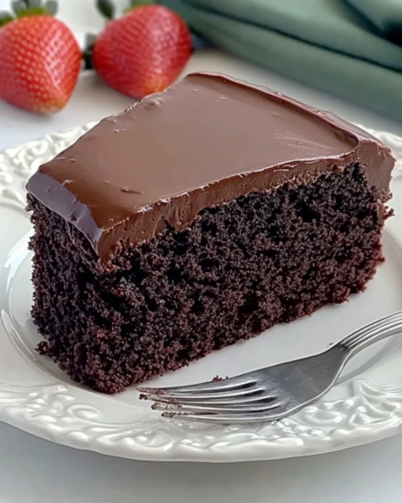 Moist chocolate cake slice with glossy chocolate buttercream frosting on white plate