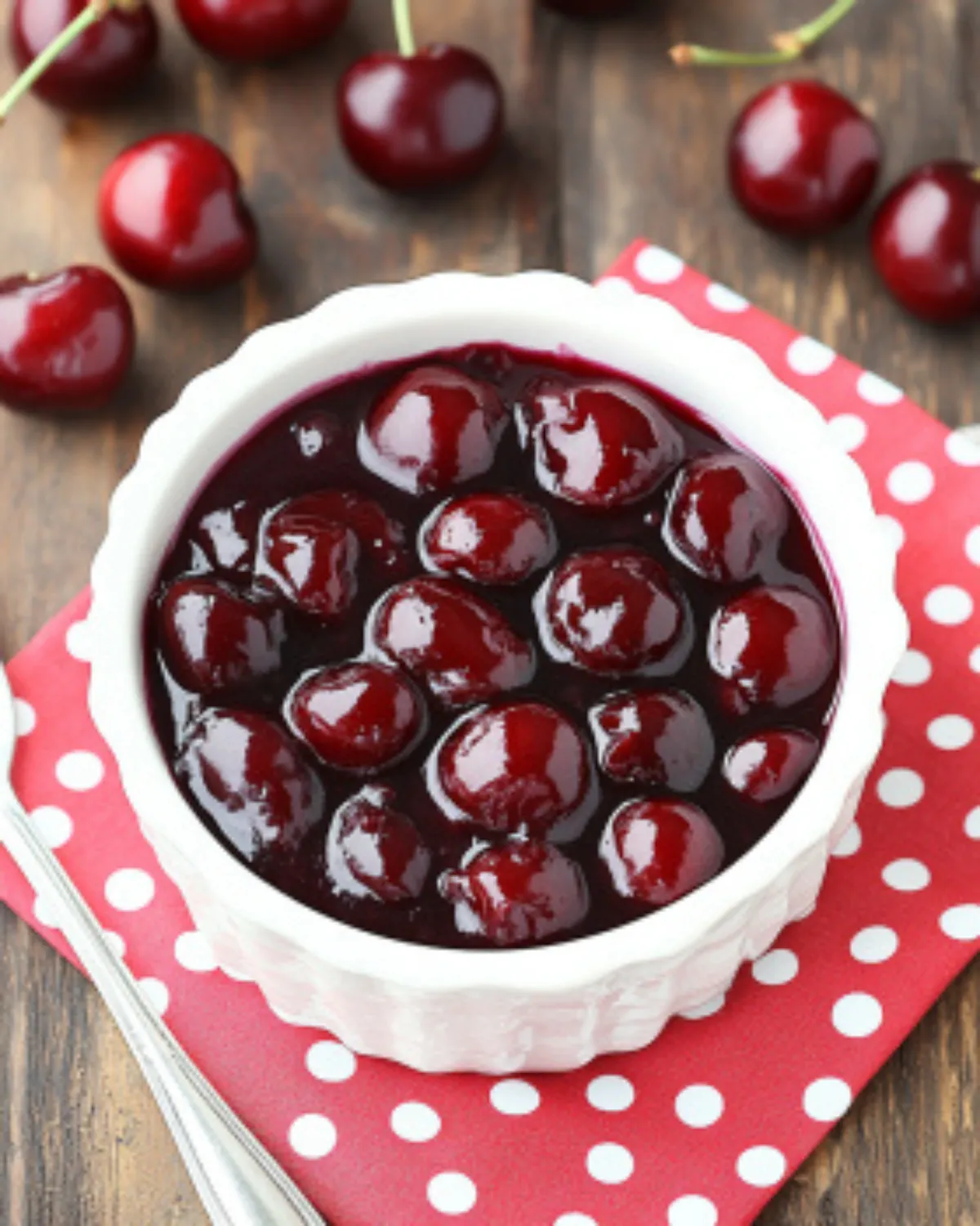 Homemade cherry pie filling in a white bowl with fresh cherries on a wooden table