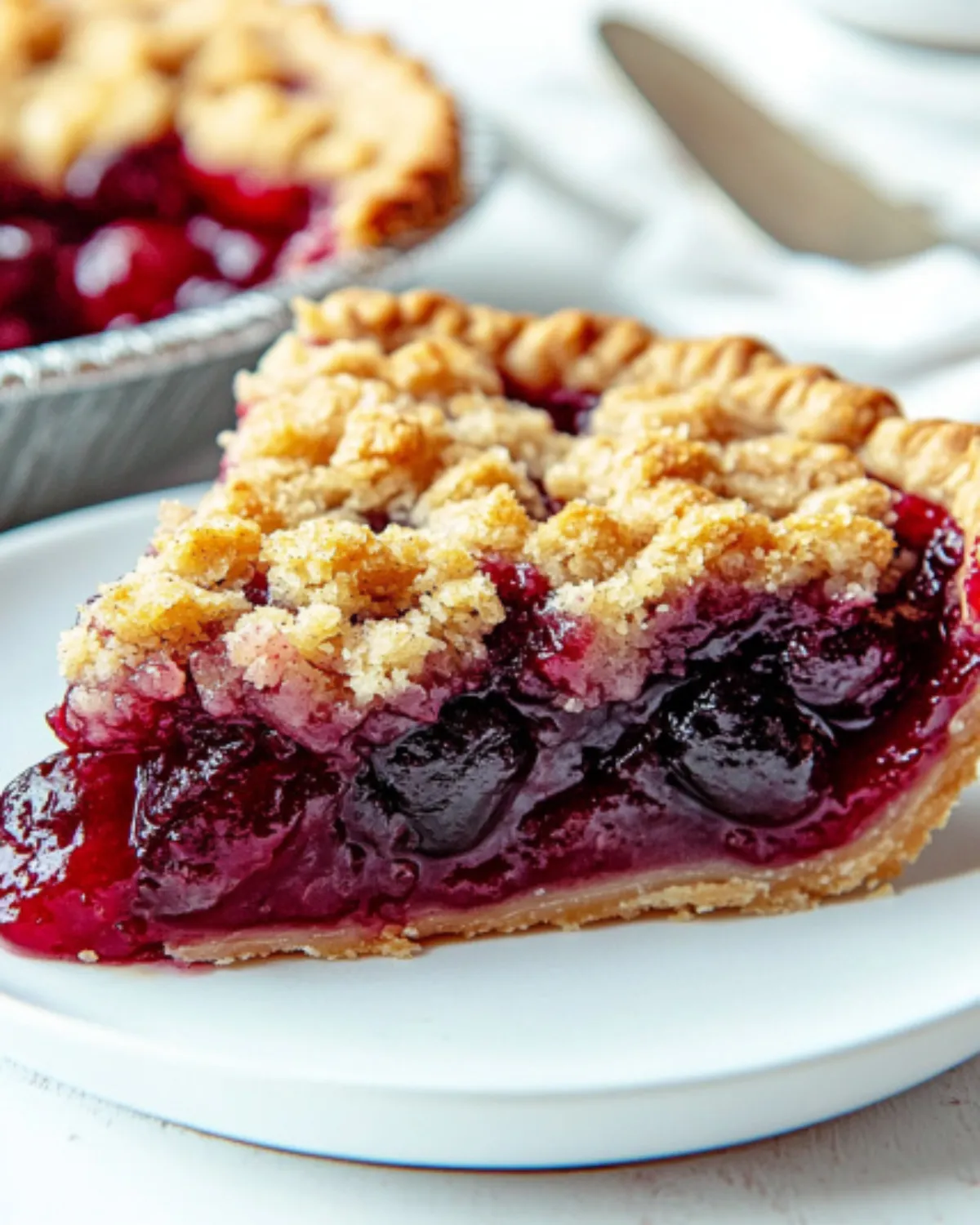 Close-up of cherry crumb pie slice with golden streusel topping and juicy cherry filling on a white plate