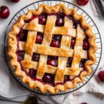 Overhead view of a freshly baked cherry pie with a golden lattice crust and bubbling cherry filling on a cooling rack.