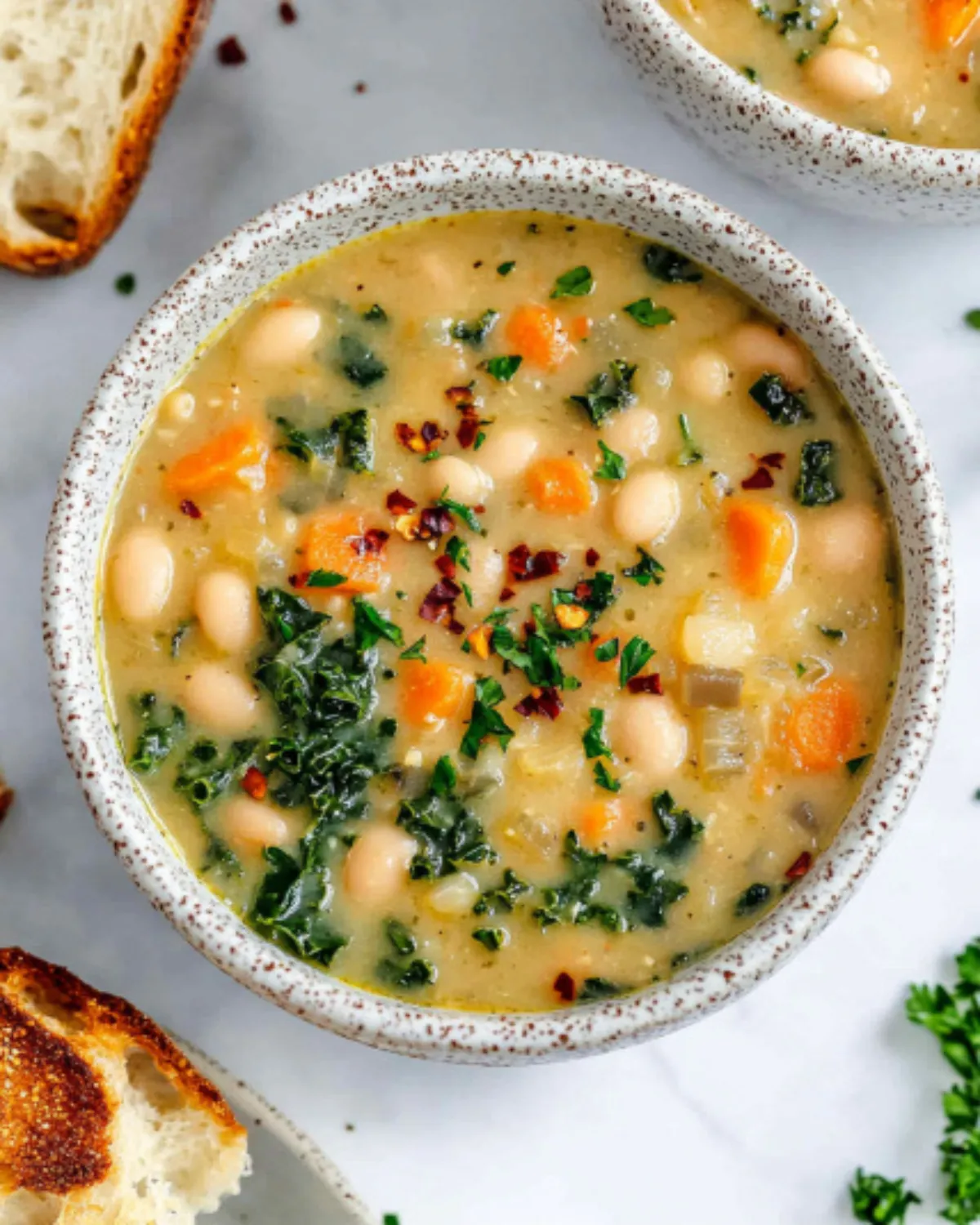 Overhead view of creamy Tuscan white bean soup with carrots and parsley, served in ceramic bowls with crusty bread