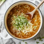 Top-down view of egg roll soup in a white Dutch oven with cabbage, ground pork, and green onions on a marble kitchen counter