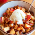 Bowl of cinnamon air fryer apples topped with vanilla ice cream on a wooden table