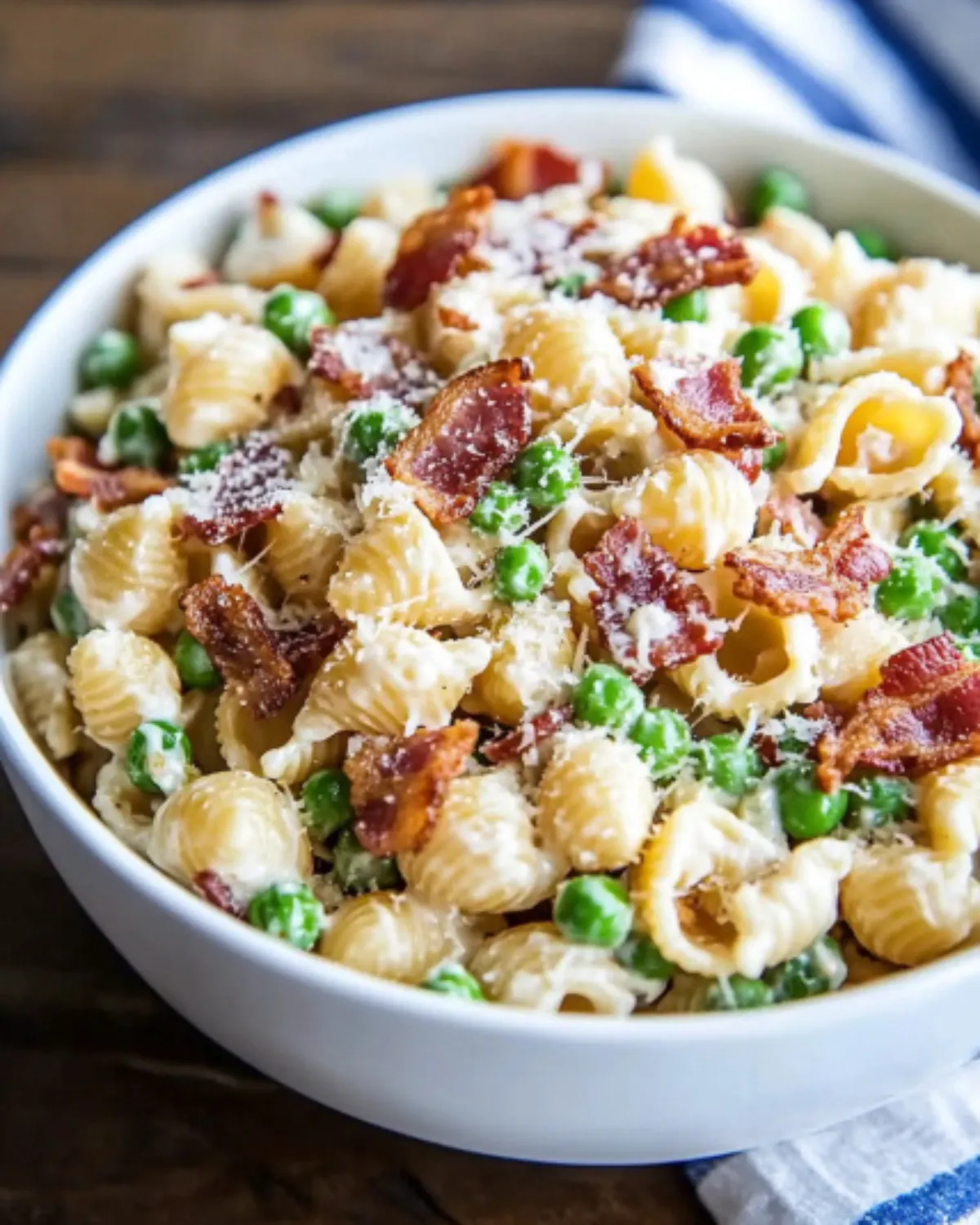 Creamy shell pasta salad with bacon, peas, and parmesan in a white bowl on a wooden table